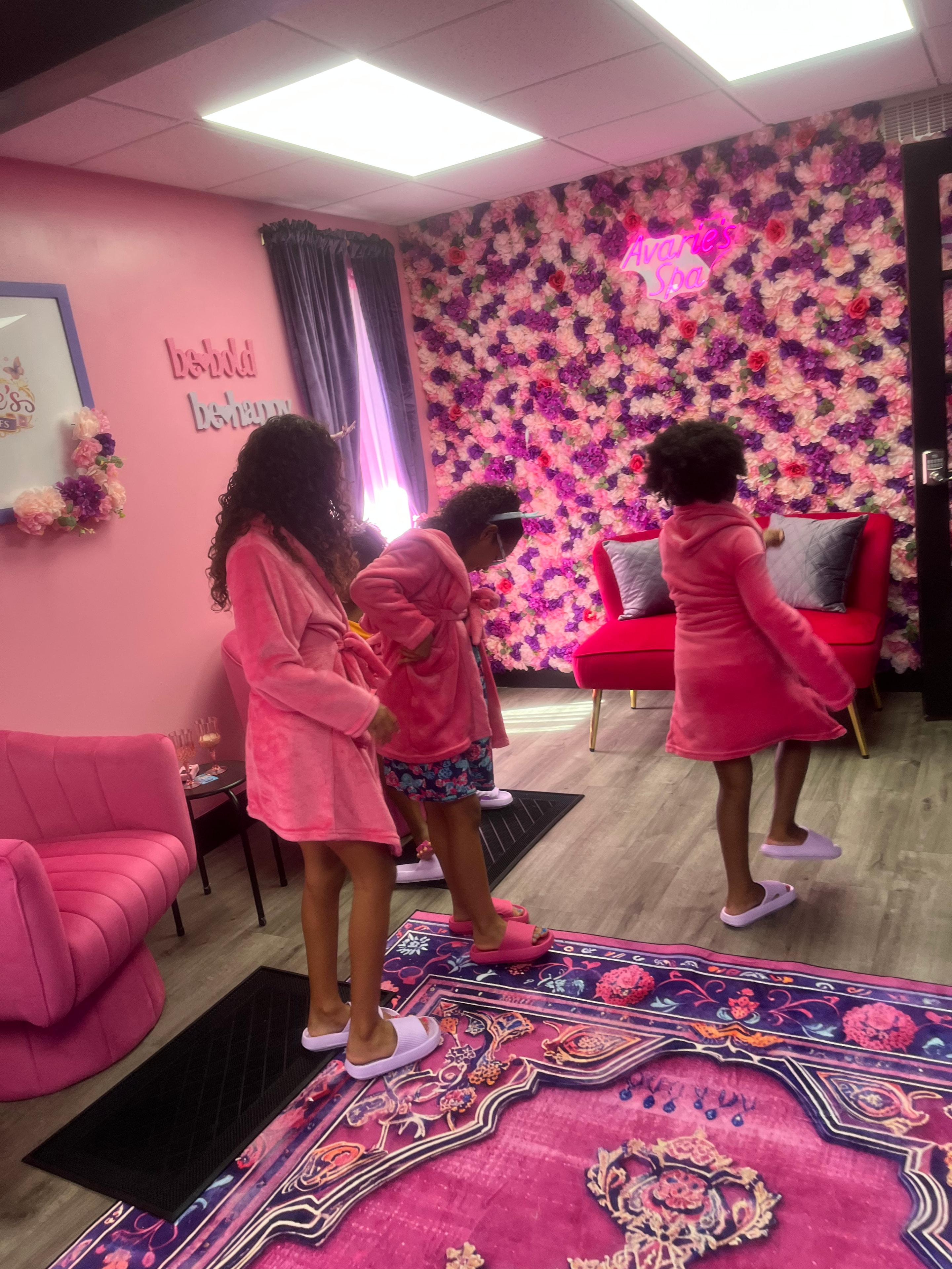 Girls in pink robes standing in the spa room with flower wall backdrop